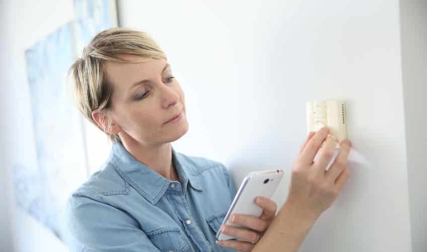 woman adjusting thermostat on wall