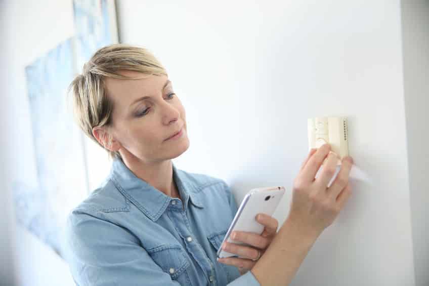 woman adjusting thermostat on wall