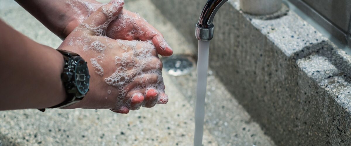 man washing hands at running faucet